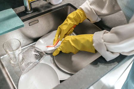 Woman in yellow gloves washing dishesの写真素材