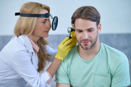 Woman otolaryngologist examining ear of middle aged man