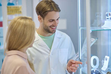Man in white coat pointing at hearing aid and woman