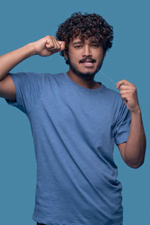 Attractive calm man flossing his teeth indoors