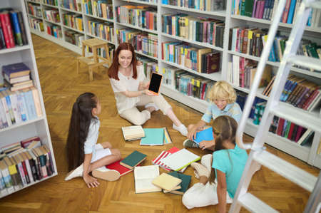 Woman showing tablet to children sitting on floor