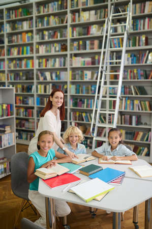 Woman standing near table with children reading