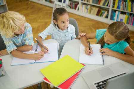 Top view of children writing at table in library