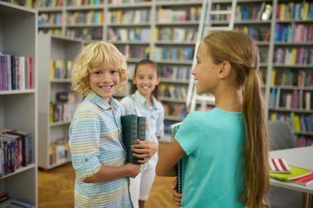 Boy with books looking at camera and two girlsの写真素材