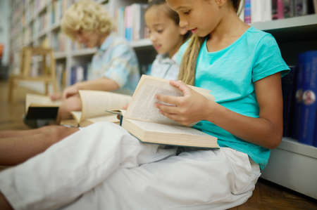 Girl leafing through book sitting with friends on floorの写真素材