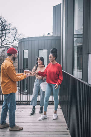 Guy treating coffee to two girls outdoors