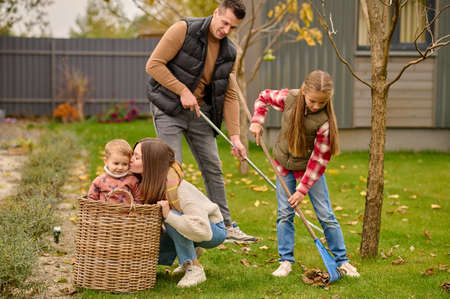 Man with girl raking leaves woman kissing child in basketの写真素材