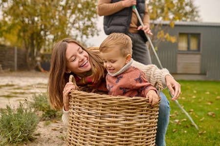 Woman playing with child sitting in basket in gardenの写真素材
