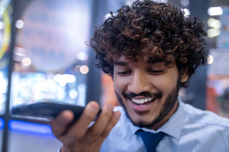 Curly-haired young businessman recording a voice message