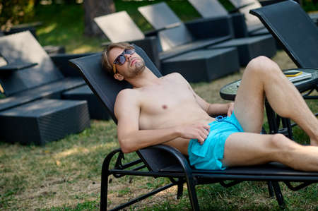 Young man lying in a chaise longue and looking relaxed