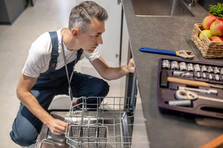 Man sitting near an open dishwasher and toolsの写真素材