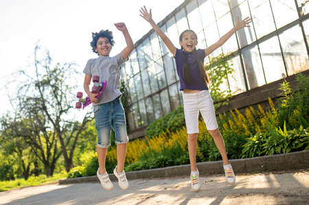 Two merry Caucasian kids jumping up outdoors