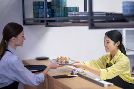 Asian waitress serving sushi to the customerの写真素材