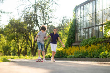 Cheerful girl teaching a boy to skateboardの写真素材