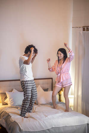 Man and woman in pajamas dancing on bed