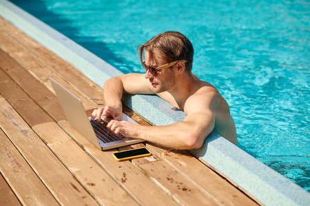 Young man at the swimming pool working on a laptopの写真素材