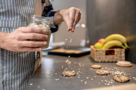 Male hand sprinkling raw biscuits with almond slices