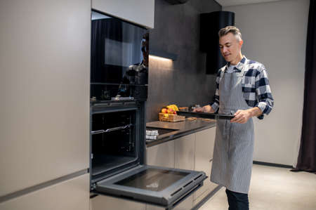 Man with baking sheet standing near open ovenの写真素材
