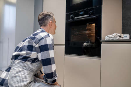 Man crouching near working oven watchingの写真素材