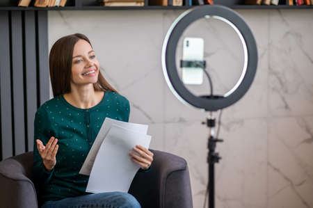 Young cute woman sitting in front of camrea and conductiong a workshop