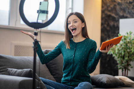 Cheerful young woman in green shirt in front of camera making online workshop
