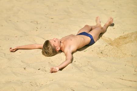 A boy sunbathing while laying on sand and looking relaxedの写真素材