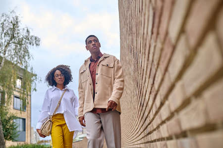 Dark-skinned man and woman walking near brick wall