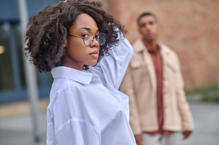 Woman touching hair looking at camera and man behindの写真素材