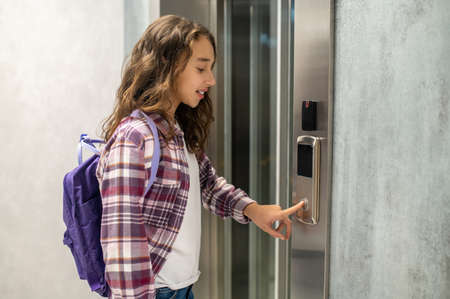 Concentrated young lady with a backpack calling the elevatorの写真素材