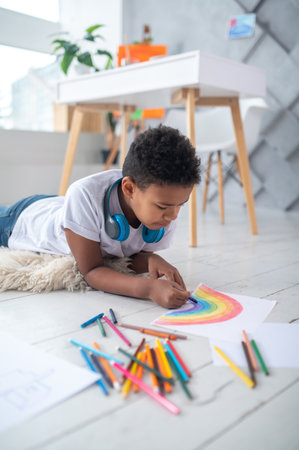 Boy painting rainbow lying on floorの写真素材