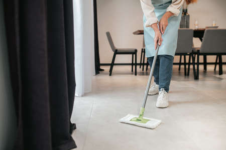 A young woman in apron cleaning the floor in the kitchen