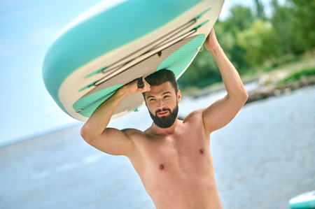 A dark-haired bearded young man carrying kayakの写真素材