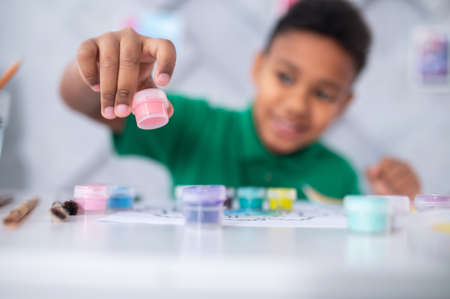 Boy stretching hand with tube of paint to camera