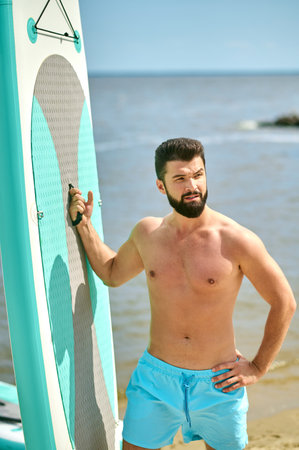 A well-built young man with a surfing board on a beachの写真素材
