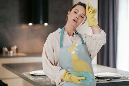 Young housewife standing in the kitchen and looking tired after cleaningの写真素材
