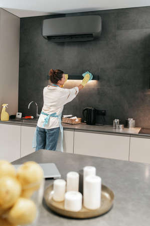 Young dark-haired woman cleaning the lamp in the kitchen