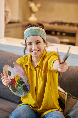 Smiling cute young woman with a palette and brushes in handsの写真素材