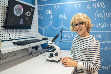 Boy in glasses looking at camera standing near microscopeの写真素材