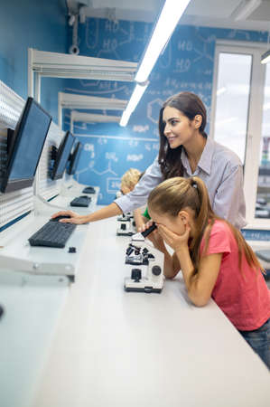 Woman looking at screen and girl leaning over microscope