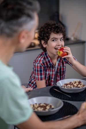 Boy with apple near mouth looking at manの写真素材