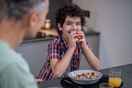 Boy eating apple looking at father at tableの写真素材