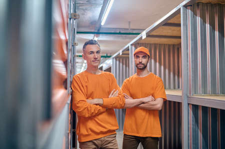 Storehouse worker and his coworker standing among storage containers