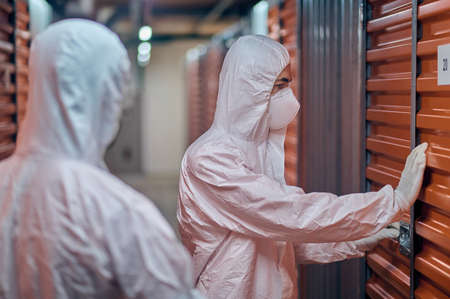 Two people in hazmat suits standing in the storehouse