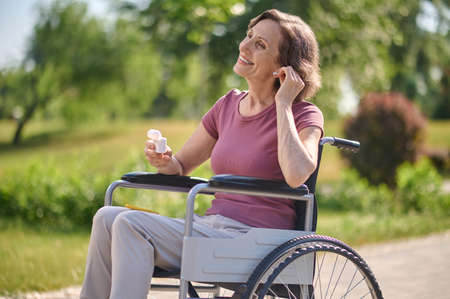 A smiling woman on a wheel-chair putting on wireless headphones