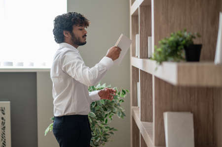 Young indian businessman choosing a book from the shelf