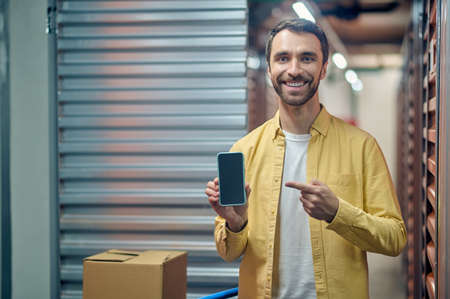 Joyful warehouse worker demonstrating his gadget before the cameraの写真素材
