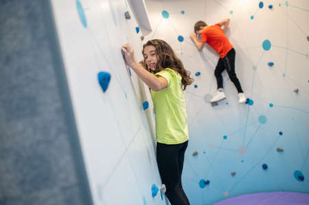 Girl and boy hanging on indoor climbing wallの写真素材