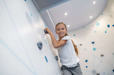 Girl smiling at camera hanging on climbing wallの写真素材