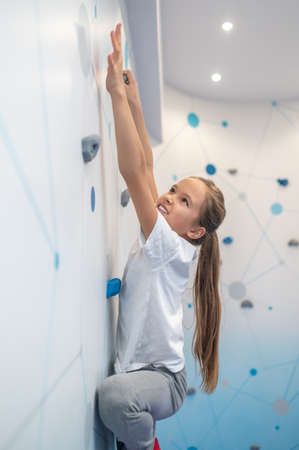 Girl stretching hand to ledge on climbing wallの写真素材