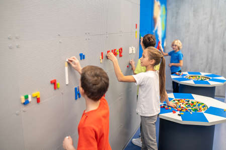 Children standing near wall making mosaic of legoの写真素材